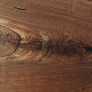 May include: Close-up of a dark brown wood grain with a knot and a natural wood finish.