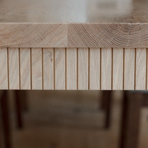 Puede incluir: Primer plano de una mesa de madera clara con un borde de listones decorativos. La superficie de la mesa es lisa y tiene una veta de madera natural.