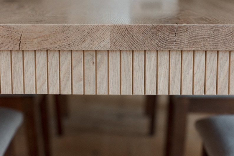 Puede incluir: Primer plano de una mesa de madera clara con un borde de listones decorativos. La superficie de la mesa es lisa y tiene una veta de madera natural.