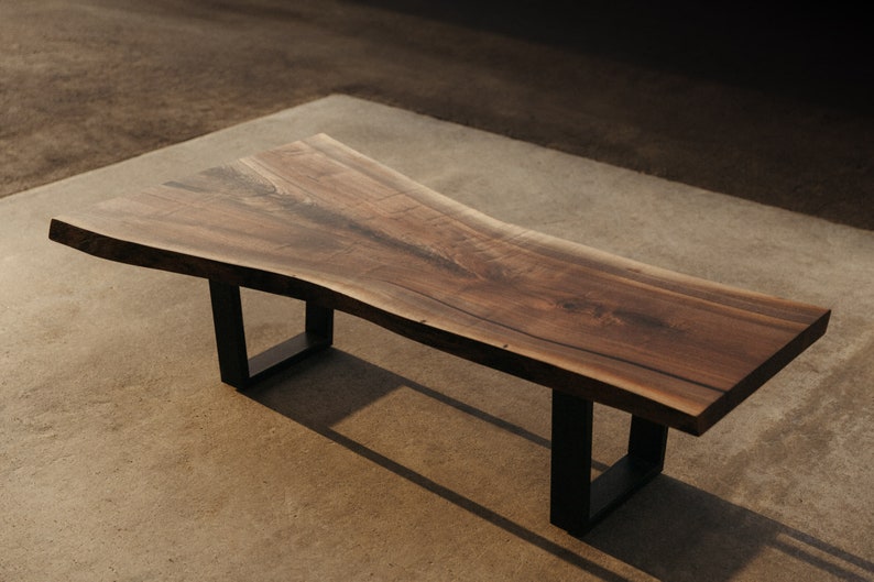 May include: A long, wooden coffee table with a live edge top and black metal legs. The table has a natural wood finish and a unique, organic shape.