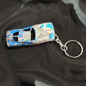 May include: A blue and silver toy car keychain with a worn paint finish. The car is attached to a silver metal key ring.
