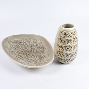 May include: A set of two ceramic dishes with a white glaze and a brown geometric pattern. The larger dish is oval shaped and the smaller dish is a vase.