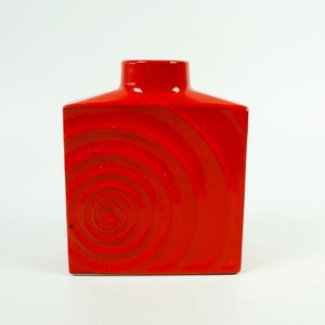 Könnte beinhalten: Eine rote Keramikvase mit quadratischer Form und einem spiralförmigen Muster.