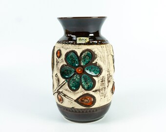May include: A brown and white ceramic vase with a floral design. The vase has a label that says "Bay Keramik".