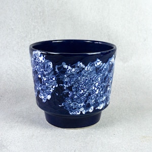 May include: A blue ceramic planter with a white and blue abstract design. The planter has a wide rim and a slightly flared base.