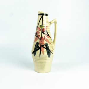 May include: A ceramic vase with a cream-coloured background and a stylised floral design in shades of red, black, and blue. The vase has a narrow neck and a wide base, and it is decorated with a textured pattern.