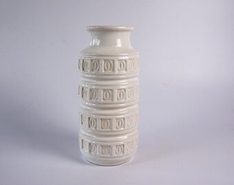 May include: White ceramic vase with a geometric pattern. The vase has a cylindrical shape and is decorated with raised circles and squares.