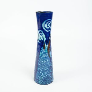 May include: A tall, blue ceramic vase with a flared top. The vase has a dark blue rim and is decorated with white and turquoise spiral designs. The body of the vase has a textured, crackle-glazed appearance in shades of blue and turquoise.