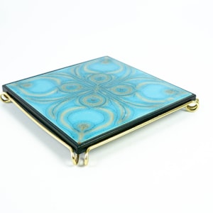 May include: A blue and gold ceramic tile with a decorative pattern is mounted on a gold metal stand. The stand has four legs that curve outwards.