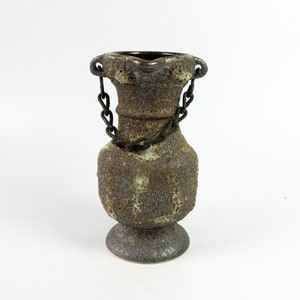 May include: A gray ceramic vase with a rough texture and a metal chain handle. The vase has a rounded body and a flared base.