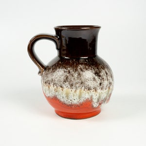 May include: A brown and orange ceramic pitcher with a white glaze. The pitcher has a rounded body and a handle.