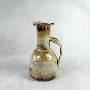 Può includere: Un'anfora in ceramica marrone e bianca con un'ampia apertura e un manico. L'anfora ha una smaltatura screziata e un aspetto rustico.