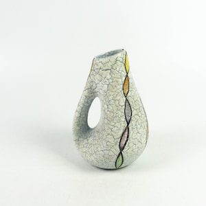 Könnte beinhalten: Eine weiße Keramikvase mit craquelé-Glasur und einem farbenfrohen geometrischen Design. Die Vase hat eine einzigartige, asymmetrische Form mit einem Henkel.