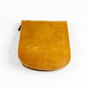 May include: A small, vintage, tan-colored leather coin purse with a rounded bottom and a black zipper. The purse has a slightly worn appearance, suggesting age and use. The stitching is visible along the edges.
