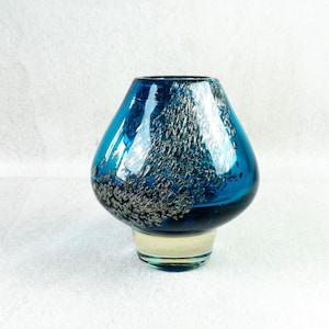 May include: A blue glass vase with a unique shape and a textured, speckled design. The vase has a clear base and a wide opening. The blue color is vibrant and eye-catching, making it a decorative piece.