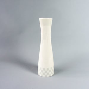 May include: A white ceramic vase with a checkered pattern around the bottom. The vase has a narrow neck and a wide base.
