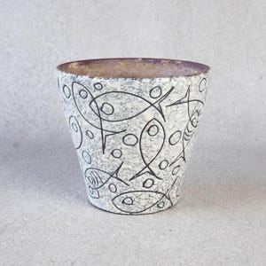 May include: A cylindrical ceramic planter with a speckled white and grey exterior. The planter is decorated with black line drawings of fish and bubbles. The interior rim is a dark brown colour.