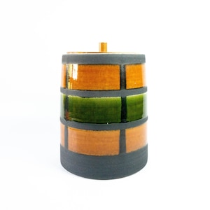Könnte beinhalten: Eine Keramikdose mit einem Holzdeckel. Die Dose ist mit einem geometrischen Muster aus orangefarbenen, grünen und schwarzen Quadraten verziert.