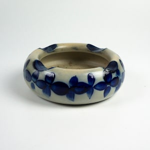 Könnte beinhalten: Ein runder Aschenbecher aus Keramik mit weißer Glasur und blauem Blumendesign. Der Aschenbecher hat eine breite, flache Schale und einen leicht erhöhten Rand.