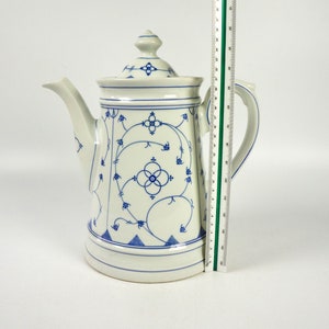 Könnte beinhalten: Eine weiße Kaffeekanne aus Keramik mit einem blauen und weißen Blumenmuster. Die Kanne hat einen Deckel und einen Ausguss.