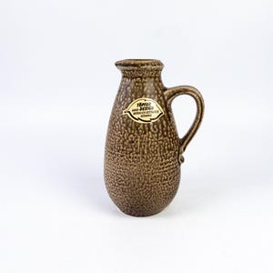 May include: A brown ceramic pitcher with a textured surface and a handle. The pitcher has a label that reads "Topper Hand-Design Handwerk Gestaltete Keramik".