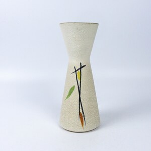 May include: A white ceramic vase with a textured surface and a geometric design in black, yellow, orange, and green.