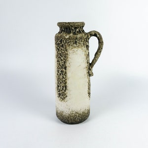 May include: A white ceramic vase with a brown speckled glaze and a handle. The vase is about 15 cm tall.