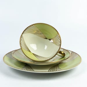 May include: A green and gold teacup and saucer set with a geometric design. The cup and saucer are made of porcelain and have a glossy finish.