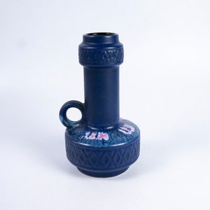 May include: A blue ceramic vase with a handle and a geometric pattern. The vase has a pink and white floral design.