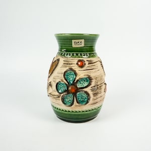 May include: A green ceramic vase with a white background and a floral design. The vase has a label that reads "BAY, KERAMIK".