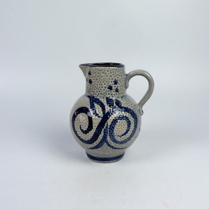 Può includere: Un'anfora in ceramica grigia con un design a spirale blu e bianco. L'anfora ha una superficie testurizzata e un piccolo beccuccio.
