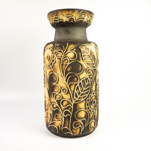 May include: A brown ceramic vase with a floral design in a light brown colour. The vase has a wide mouth and a narrow base.