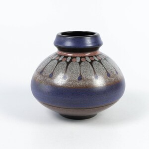 Könnte beinhalten: Eine kleine, runde Keramikvase mit dunkelblauer Glasur und einem dekorativen Muster in Braun-, Rosa- und Weißtönen.