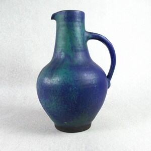 Peut inclure: Un pichet en céramique bleu et vert avec une base large et une anse. Le pichet a un glaçage marbré.
