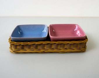 May include: A wicker serving tray with two square ceramic bowls, one blue and one pink.