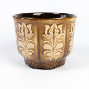 May include: A brown ceramic planter with a decorative floral design in a lighter shade of brown.