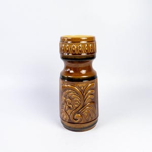 May include: A brown ceramic vase with a floral design. The vase has a wide mouth and a narrow base. It is decorated with a brown and black floral pattern.