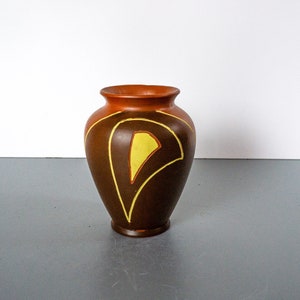 May include: A brown ceramic vase with a geometric design in yellow and orange. The vase has a rounded body and a narrow opening.