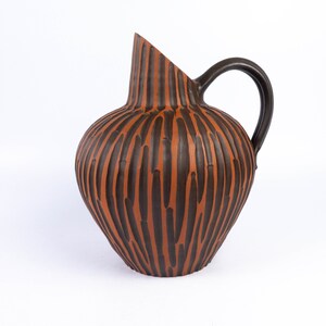 May include: A brown and black ceramic jug with a textured, striped design. The jug has a wide base and a narrow neck.