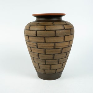 May include: A brown ceramic vase with a brick pattern design. The vase has a rounded body and a slightly flared opening.