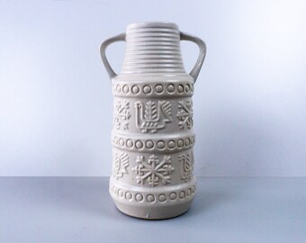 May include: A white ceramic vase with two handles and a geometric pattern. The pattern includes snowflakes, birds, and circles.