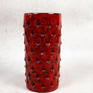 May include: A cylindrical red ceramic vase with a textured surface. The vase has a series of teardrop-shaped indentations across its surface. The vase is a decorative item, suitable for holding flowers or as a standalone art piece.