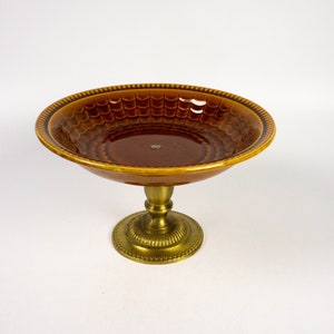 Könnte beinhalten: Eine braune Keramik-Fußschale mit strukturierter Innenseite und dekorativem Rand. Die Schale steht auf einem messingfarbenen Metallsockel mit detailliertem, kreisförmigem Fuß. Vintage und dekoratives Design.