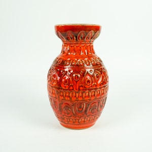 May include: Orange ceramic vase with an intricate embossed design. The vase has a wide mouth and a rounded body.