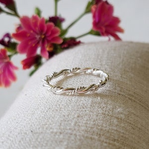 Könnte beinhalten: Ein silberner Ring mit gedrehtem Band. Der Ring ist schlicht und zart, mit einer glatten, polierten Oberfläche.