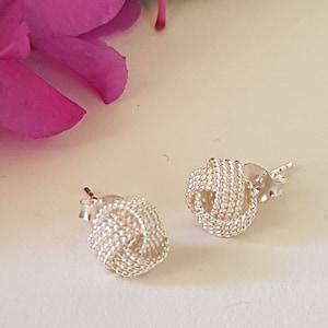 May include: A pair of silver knot-shaped stud earrings. The earrings are made of a delicate, woven design.