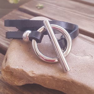 May include: A black leather bracelet with a silver toggle clasp. The bracelet is wrapped twice around the wrist.
