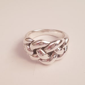 Könnte beinhalten: Ein silberner Ring mit einem geflochtenen Design. Der Ring ist dick und hat eine breite Band.
