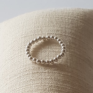 Könnte beinhalten: Ein silberner Perlenring mit schlichtem Design. Der Ring besteht aus kleinen, runden Perlen, die gleichmäßig verteilt sind.