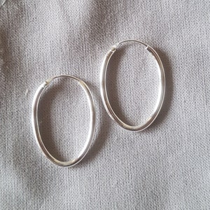 Könnte beinhalten: Zwei silberne Creolen, beide oval geformt und mit glatter Oberfläche.